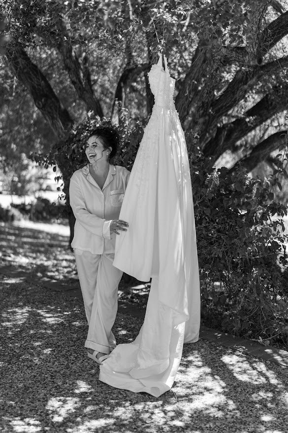 Bride laughing beside her hanging wedding dress