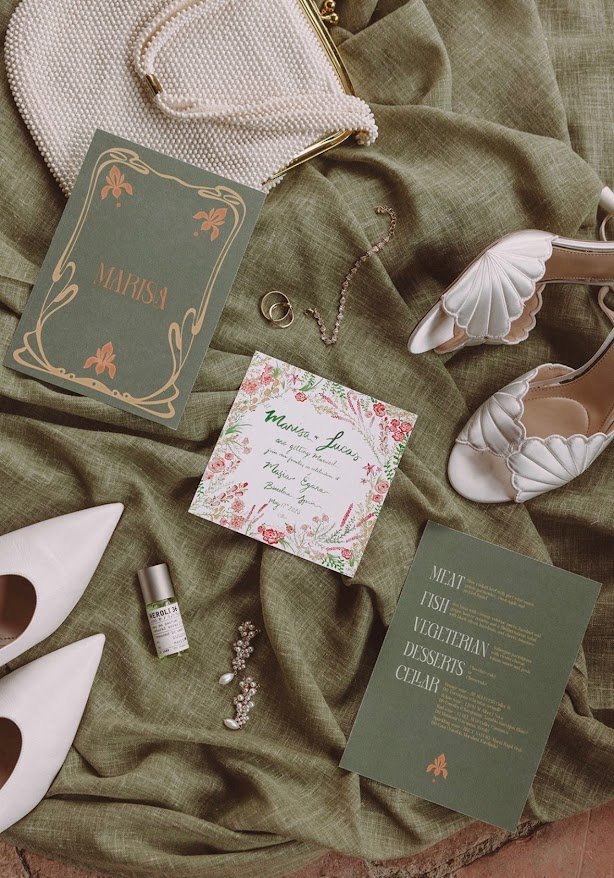 Flat lay of invitations, shoes and details on green linen