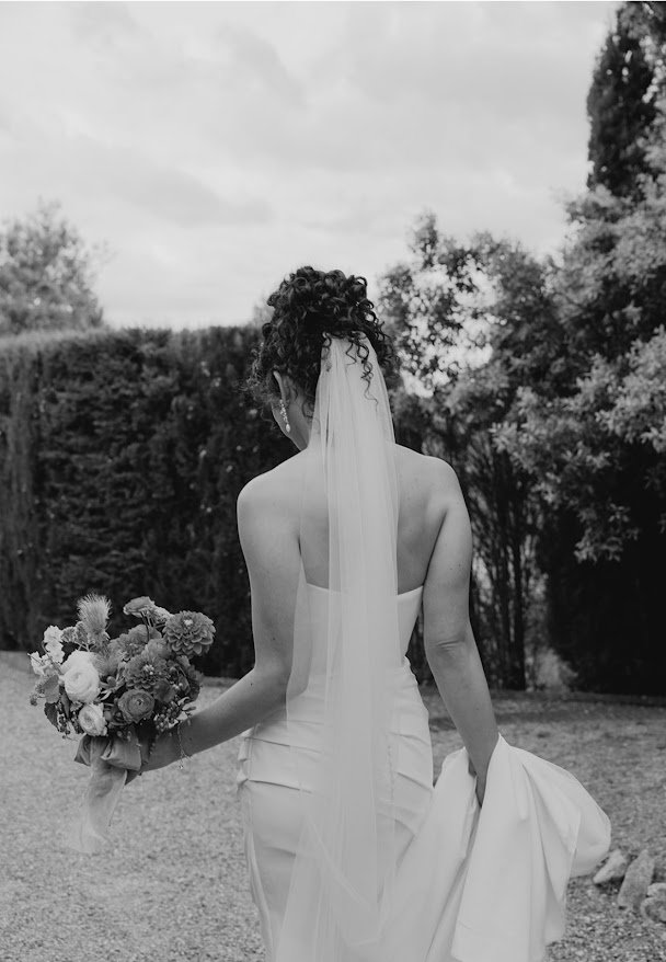 Bride from behind holding her bouquet, veil flowing